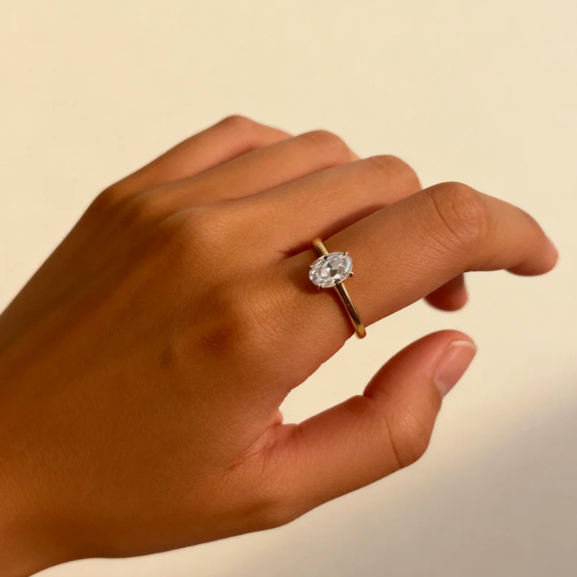 Gold oval moissanite four-prong solitaire ring worn on finger, minimalist engagement jewelry for women