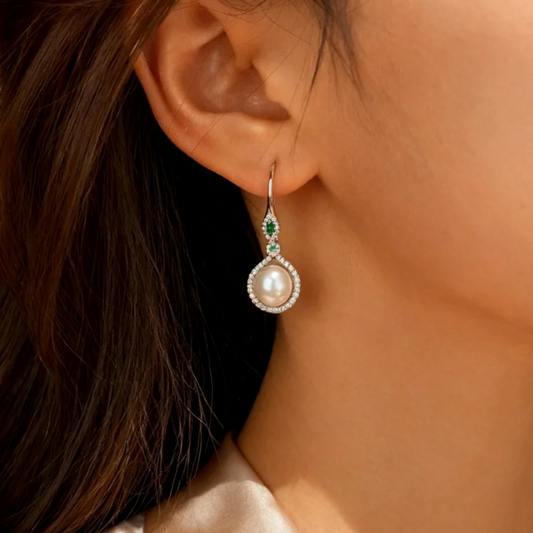 Silver pearl drop earring with emerald accents worn on ear, elegant hook style jewelry for women